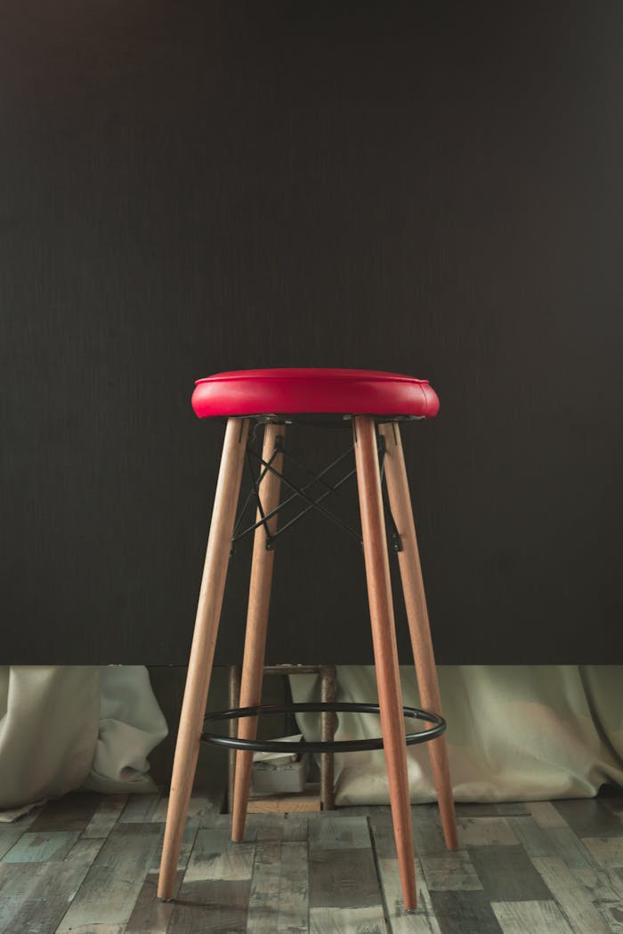 Stylish wooden stool with a red leather cushion against a dark background, perfect for modern interiors.